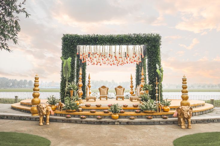 Lakeside mandap at dusk with gold pillars, elephant figures and a greenery arch by RAW Group